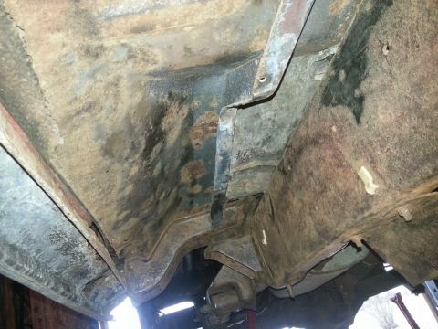 1984 Ford Bronco - Underbody photo of a vehicle floor pan and frame rail with surface rust and old undercoating, not a document.