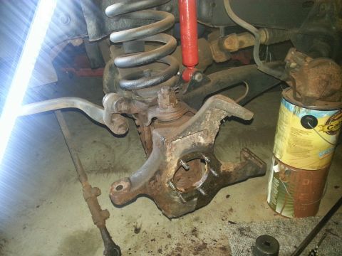 1984 Ford Bronco - Photograph of a front steering knuckle, coil spring and shock with a grease can during suspension work, not a document.
