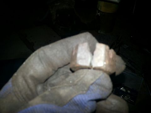 1984 Ford Bronco - Dark photograph of a gloved hand holding a worn set of brake pads, not a document.