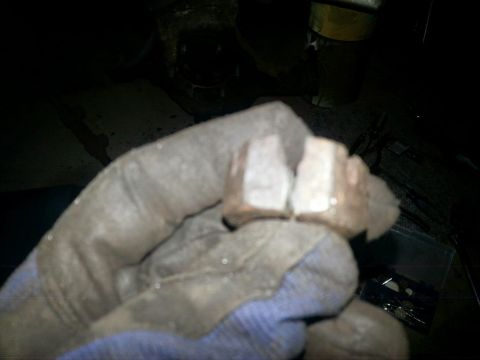 1984 Ford Bronco - Dark photograph of a gloved hand holding a worn set of brake pads, not a document.