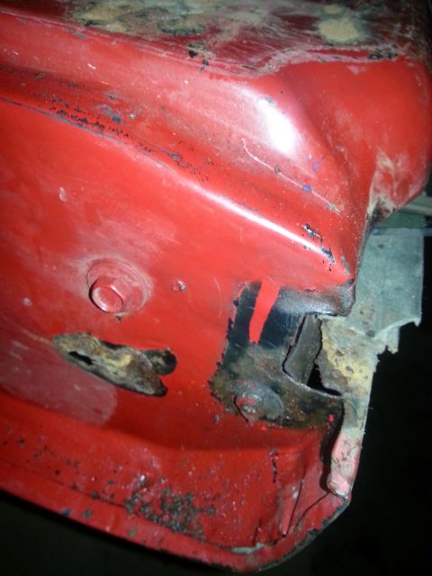1984 Ford Bronco - Photograph of a rusty red sheet-metal body panel with corrosion holes near a body seam, not a document.
