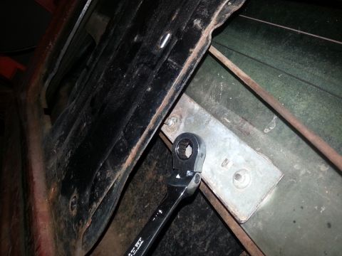 1984 Ford Bronco - Photograph of a ratcheting wrench on a body-mount bracket on a vehicle floor pan during repair, not a document.