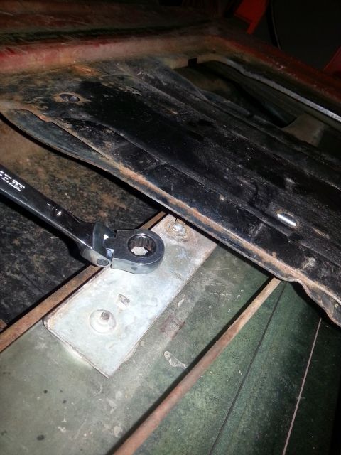 1984 Ford Bronco - Photograph of a ratcheting wrench on a body-mount bracket on a vehicle floor pan during repair, not a document.