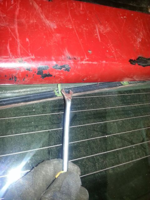 1984 Ford Bronco - Photo of a tool worked along the rear window trim of a red vehicle, not a technical document.