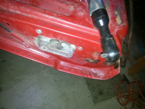 1984 Ford Bronco - Photo of a striker plate being removed from a red vehicle panel with an air ratchet, not a document.