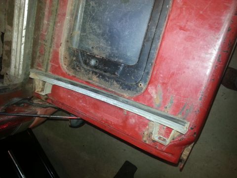 1984 Ford Bronco - Photo of a red vehicle panel with a window opening and trim strip, not a technical document.