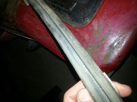 1984 Ford Bronco - Photo of a hand holding a metal trim molding by a red vehicle panel, not a document.