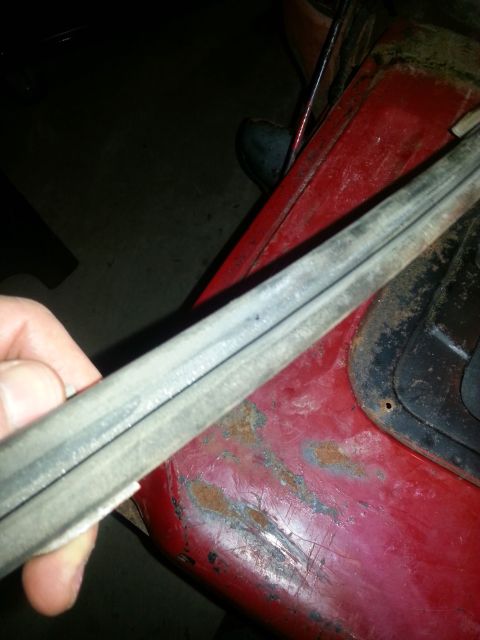 1984 Ford Bronco - Photo of a hand holding a metal trim strip above a red vehicle panel, not a document.