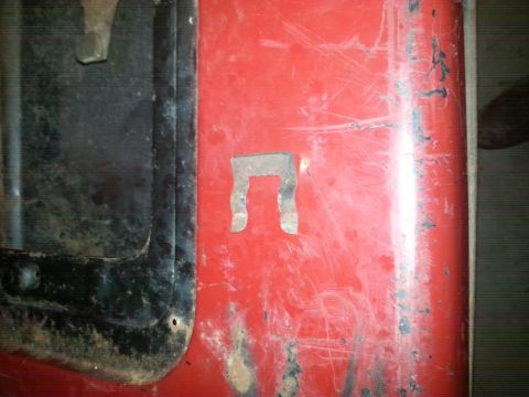 1984 Ford Bronco - Photo of a scratched red vehicle panel with a bracket cutout, not a document.