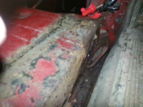 1984 Ford Bronco - Photo of a corroded red vehicle rocker and frame section, not a document.