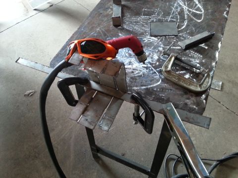 1984 Ford Bronco - Photograph of a plasma/cutting tool and clamped metal pieces on a welding table, not a document.