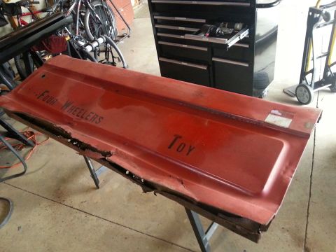 1984 Ford Bronco - Photograph of a red pickup tailgate with painted text resting on a shop table, not a document.