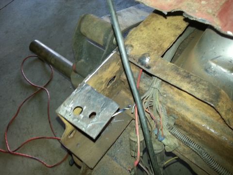 1984 Ford Bronco - Photograph of a fabricated steel bracket held in a bench vise next to a vehicle frame and wiring.