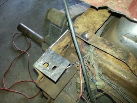 1984 Ford Bronco - Photograph of a fabricated steel bracket held in a bench vise next to a vehicle frame and wiring.