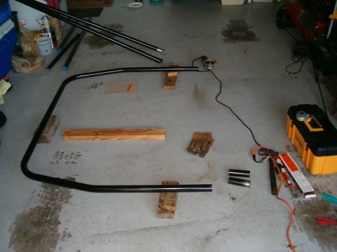 1979 Ford Bronco - Metal tubing and welding supplies are staged on a concrete floor, suggesting fabrication work is underway.