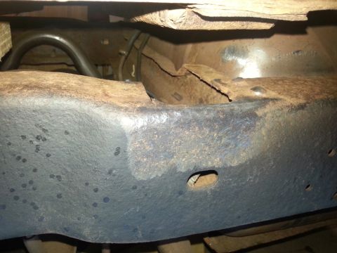 1984 Ford Bronco - The underside of a vehicle shows significant rust and damage to a pipe.