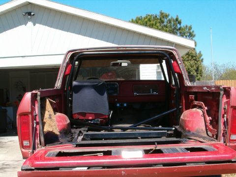1979 Ford Bronco - The rear of a red pickup truck is shown, a roll cage and an open bed with missing components.