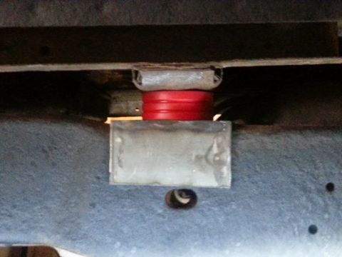 1984 Ford Bronco - A red suspension bushing is visible between two metal brackets on the underside of a vehicle.