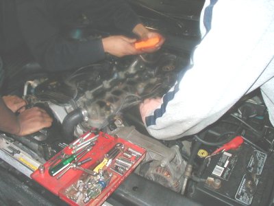 1997 Ford Taurus - Mechanics work on a car's engine bay, with a red toolbox and battery visible.