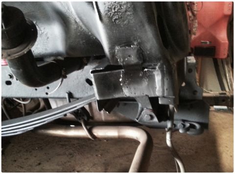 1984 Ford Bronco - Photograph of a freshly painted truck frame section with leaf spring and exhaust pipe in a shop.