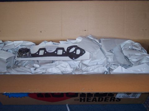 1990 Ford Bronco - A new exhaust manifold and gasket are packed in a box with protective paper.