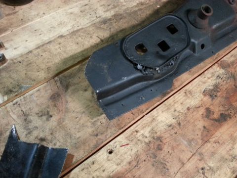 1984 Ford Bronco - Workshop photo of a painted sheet-metal body bracket resting on a wood bench, not a technical document.