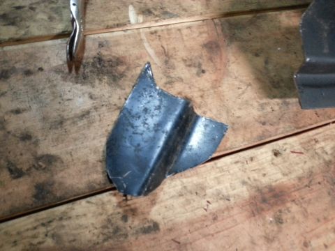 1984 Ford Bronco - Workshop photo of a small fabricated sheet-metal bracket on a wood bench, not a technical document.