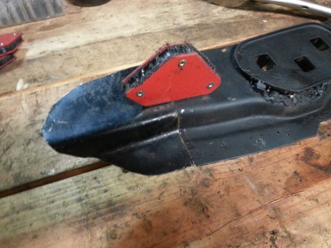 1984 Ford Bronco - Workshop photo of a sheet-metal body bracket with a welding magnet attached, not a technical document.