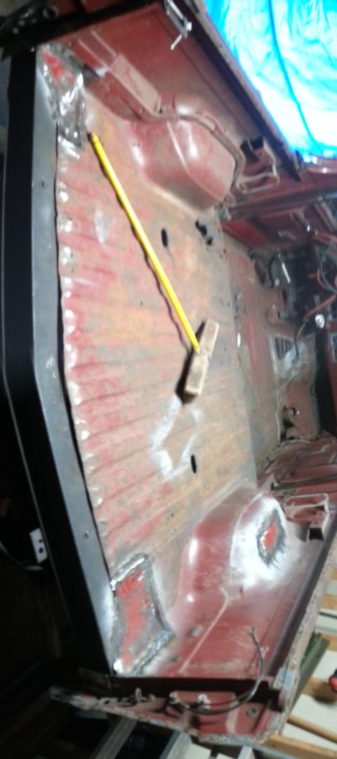 1984 Ford Bronco - Workshop photo of a red cab floor pan with a measuring stick laid across it, not a technical document.