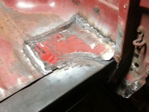 1984 Ford Bronco - Workshop close-up of a fresh welded floor patch beside a body mount, not a technical document.