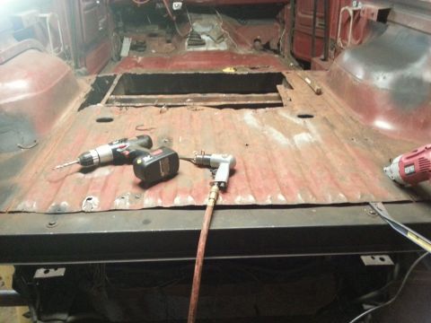 1984 Ford Bronco - Photo of a rusty truck floor pan with a cutout opening and drills during a restoration project.