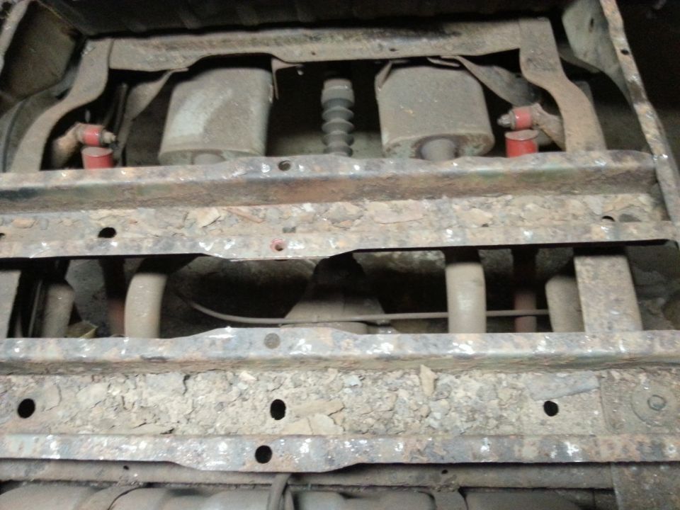Underside view of vehicle frame crossmembers and rusty floor structure