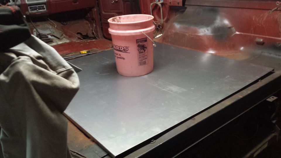 Sheet of metal laid across a truck bed area with a paint bucket on top in a garage