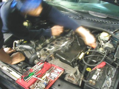 1997 Ford Taurus - A mechanic works on a vehicle's engine bay, with a toolbox full of tools nearby.