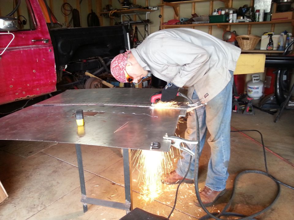 Person grinding or cutting a large metal panel on a table with sparks flying in a garage