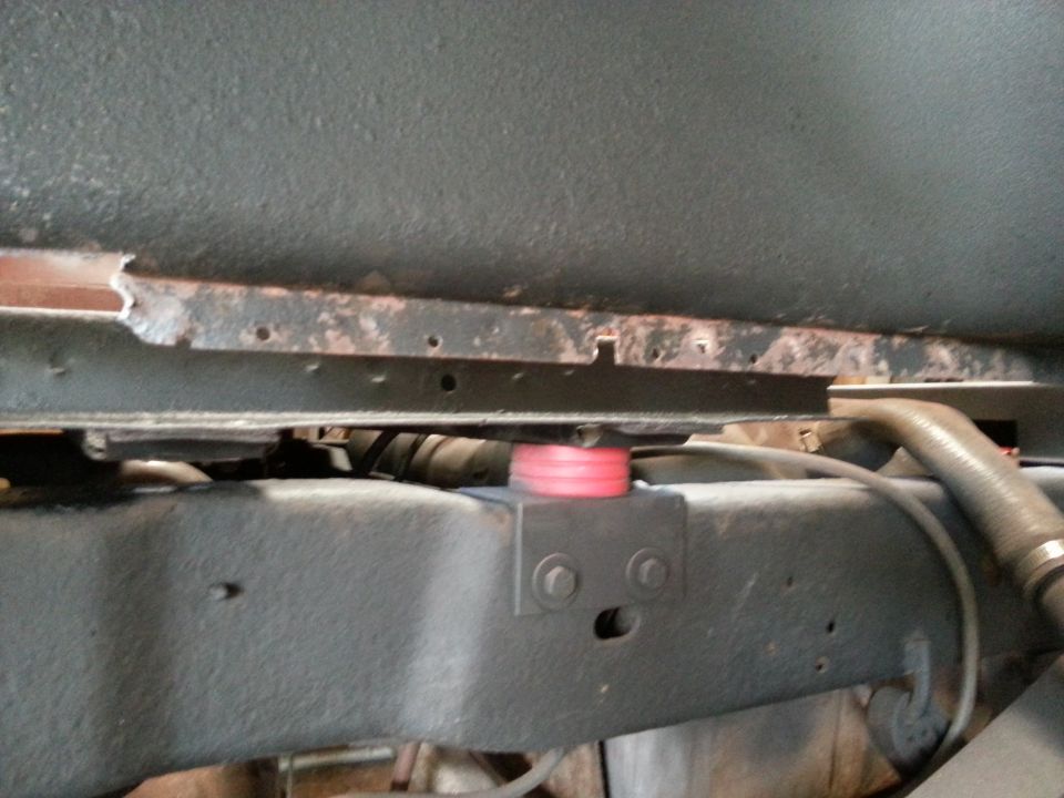 Vehicle frame rail and rocker area from below with a pink bushing visible
