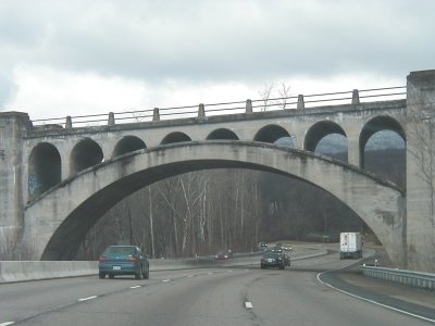 1997 Ford Taurus - A concrete bridge with multiple arches spans a highway carrying traffic under a cloudy sky.