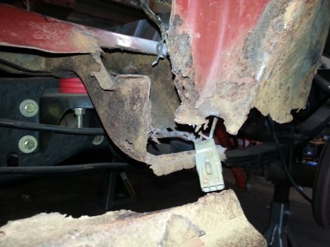 1984 Ford Bronco - Undercarriage photo showing rusted body metal and a wiring connector, not a technical document.