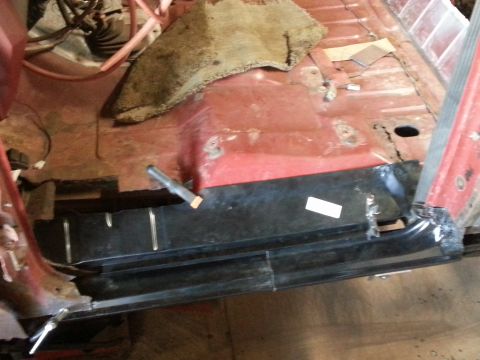 1984 Ford Bronco - Photo of a vehicle floor interior showing rust and a black rocker reinforcement panel being fitted during repair.