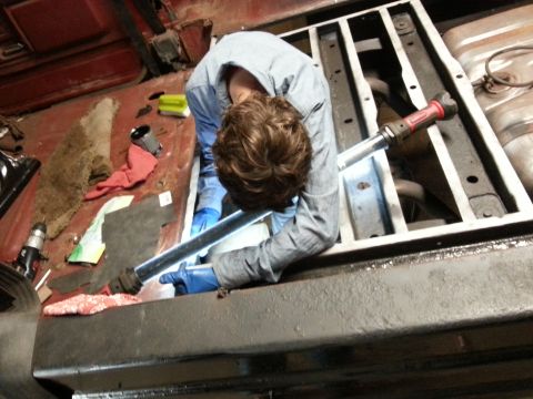 1984 Ford Bronco - Photo of a person working with a long bar over a vehicle floor pan during a frame restoration.