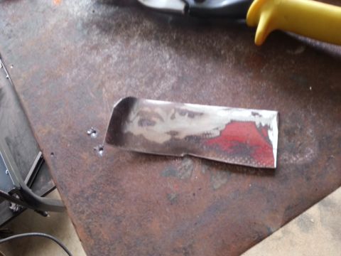 1984 Ford Bronco - Photo of a small bare-metal patch piece lying on a rusty steel workbench next to pliers.