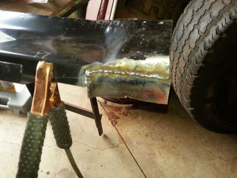 1984 Ford Bronco - Photo of a fresh weld bead joining a black body panel, with a welding ground clamp attached.