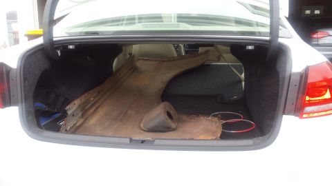 1984 Ford Bronco - Photo of a rusty removed floor pan and metal panel laid inside the trunk of a white car.