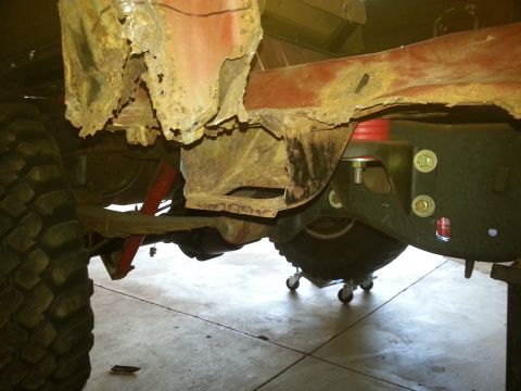 1984 Ford Bronco - Photo of a corroded vehicle underbody and frame in a garage, not a technical document.