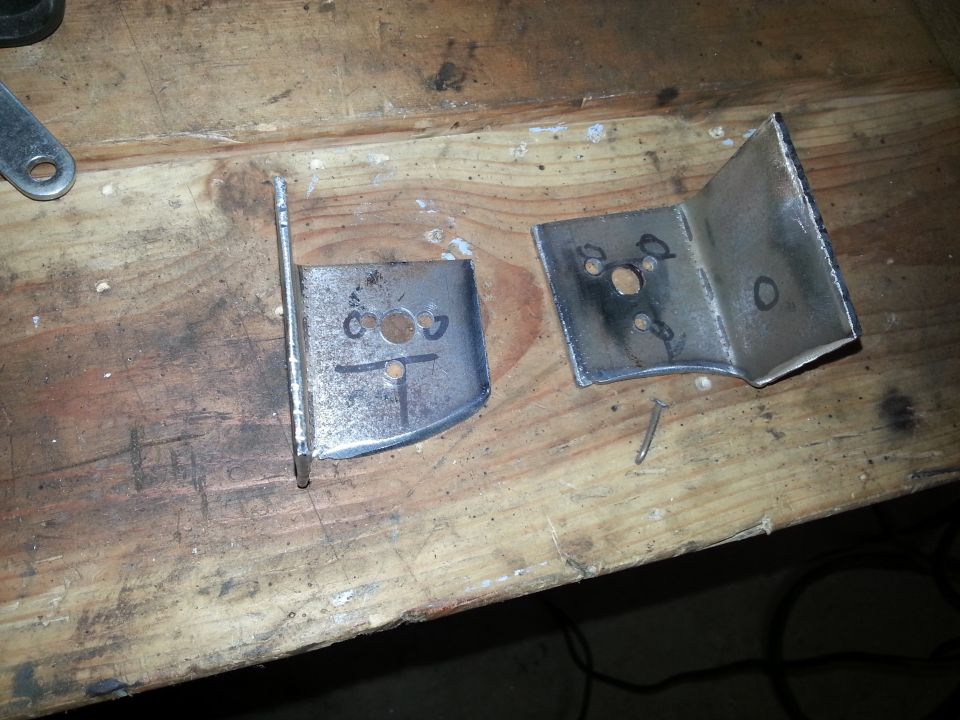 Two fabricated steel mounting brackets on a wooden workbench