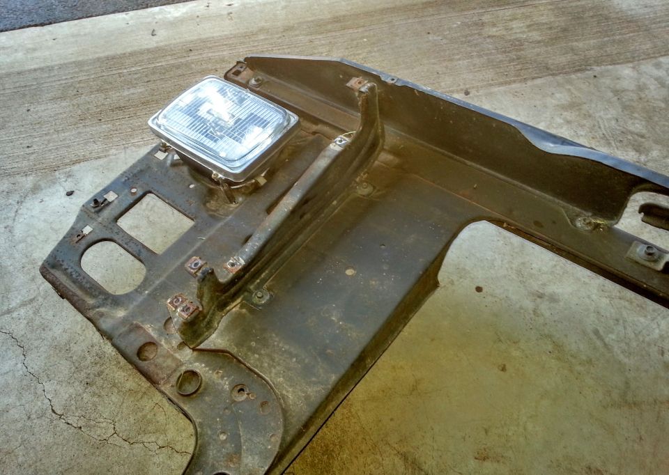 Corner of a removed radiator support with one sealed-beam headlight