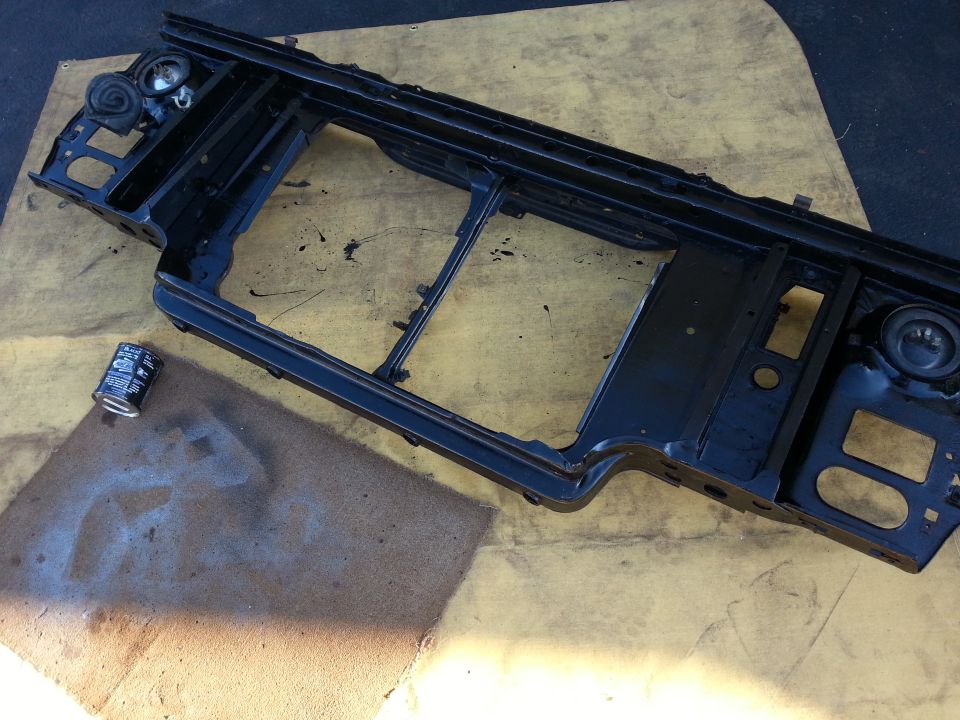 Painted black radiator core support panel resting on cardboard on a workbench