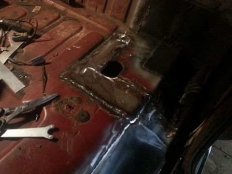 Welded floor pan patch with access hole over a red painted truck floor