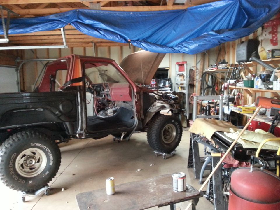 Project pickup truck under a tarp in a cluttered home garage workshop