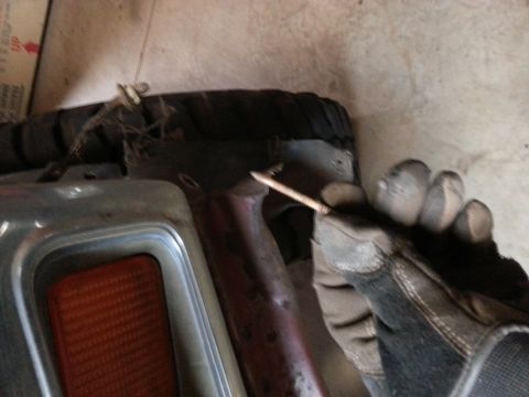 Gloved hand holding a screw beside a tire and a vehicle's chrome/amber side marker light